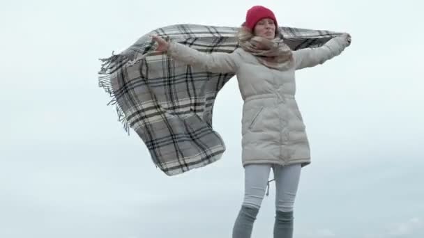 Egy fiatal nő a meleg ruhát áll ellen az égen, tartja a takarót a kezében — Stock videók