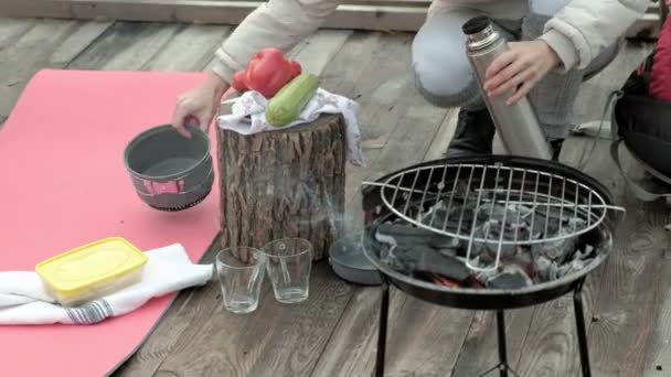 Una turista en el puente junto al río con una mochila, un perro corre a su lado, cocina comida a la parrilla, corta verduras, un picnic, actividades al aire libre y un estilo de vida saludable. concepto de viaje, cerca — Vídeos de Stock