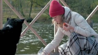 Nehir kıyısında bir sırt çantası ile yakın bir köprü üzerinde sıcak giysiler içinde bir kadın turist ızgara sebzeler hazırlar, yiyor ve beslemek köpek, piknik, Aktif istirahat, sağlıklı bir yaşam tarzı. Seyahat kavramı