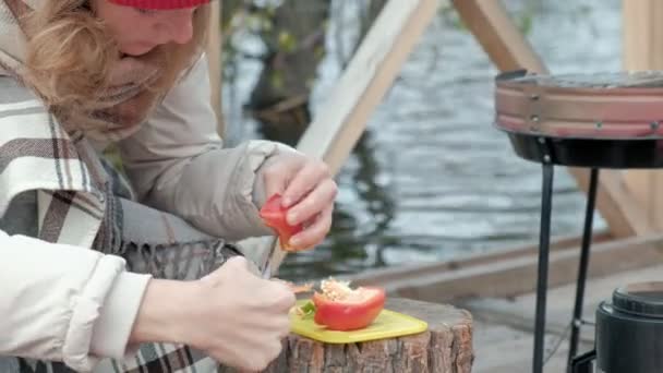 Woman tourist in warm clothes on a bridge near the river bank with a backpack, sieves vegetables, preparing food on the grill, picnic, active rest, healthy lifestyle. Travel concept — Stock Video