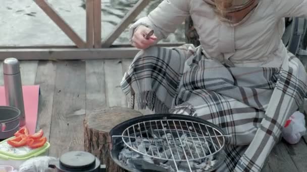 Woman tourist in warm clothes on a bridge near the river bank with a backpack, sieves vegetables, preparing food on the grill, picnic, active rest, healthy lifestyle. Travel concept — Stock Video