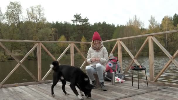 Uma turista se senta na ponte perto da margem do rio, alimenta o cão, cozinha comida, piquenique, descanso ativo e estilo de vida saudável ao ar livre nas montanhas de verão e natureza marinha. Bela inspiração — Vídeo de Stock