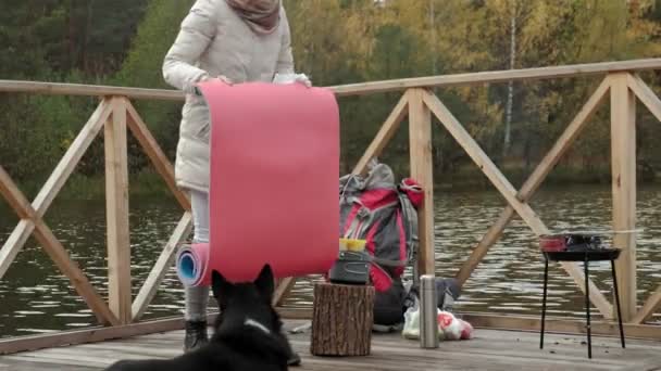 Žena turistické na mostě poblíž břehu řeky bere věci mimo její batoh, šíří turistické koberec, vedle ní je pes, piknik, Outdoorové aktivity a zdravého životního stylu. cestovní koncept — Stock video