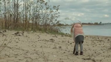 sıcak giysiler, kıvırcık saçlı kız çalışır, sahilde kahverengi bir köpekle oynar, onu bir sopa, soğuk hava atar