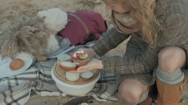 Genç kadın bir ceket nehrin okyanus plaj oturur, piknik, aşçılar et ve sebze ızgara vardır, Doğa, soğuk hava hamburger toplar