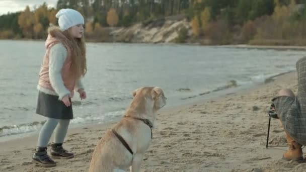 Genç kadın bir ceket ve kıvırcık saçlı, Anne kızı, olan bir kız nehir kıyısında sahilde otururken, okyanus, vardı et ve sebze ızgara, bir köpekle oynamayı bir kız yemek bir piknik — Stok video