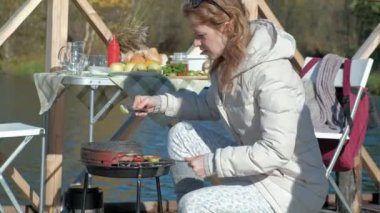 sebze ve et ızgara, bir hamburger hazırlama hazırlanıyor genç kadın sıcak giysiler içinde piknik Nehri üzerinde yakın, oynayan bir köpek banka bir ahşap köprü, bir hafta sonu, soğuk hava, açık üzerinde
