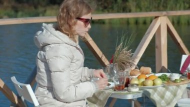 masada oturan, çay içme, reçel, bir ahşap köprü, hafta sonu, soğuk hava, kamp, turizm nehir kıyısında piknik ile pancakes yemek sıcak güneş gözlüğü, Genç kadın