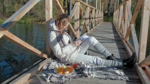 在秋河附近的桥上 一位女士看书 喝着茶4K — 图库视频影像