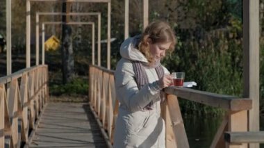 bir kadın sonbahar Nehri yakınında köprüde bir kitap okur ve çay içer