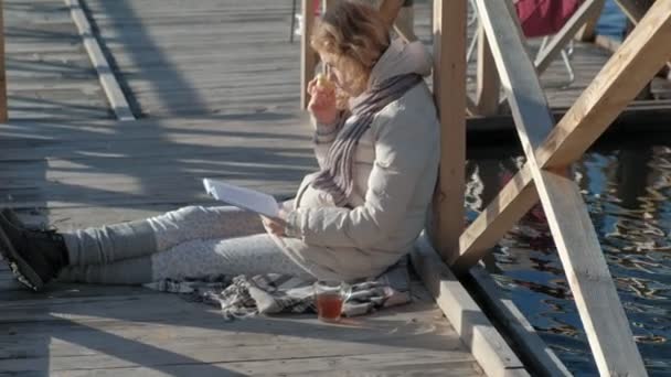 Vrouw op de brug in de buurt van de rivier in de herfst een boek leest en eet een appel — Stockvideo