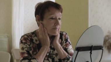 Yaşlı bir kadın kırışıklıkları aynaya bakar. Deriyi düzgünleştirir. Plastik cerrahi ve Kollajen enjeksiyonları. Kendi kusurları ile gerçekçi görüntüler.
