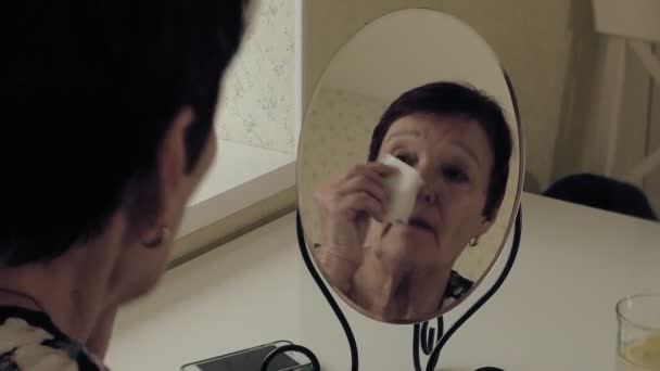 Una vecchia donna guarda le rughe nello specchio. Pulisce la pelle dai cosmetici. Cura del viso. Chirurgia plastica e iniezioni di collagene. Immagini realistiche con le proprie imperfezioni . — Video Stock
