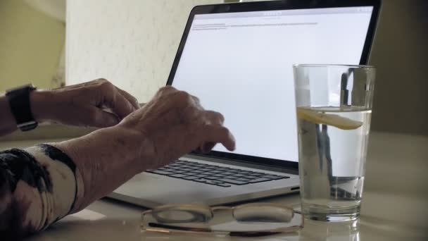 En gammal kvinna sitter vid bordet, en kosmetisk vävnad mask appliceras på hennes ansikte. Hon använder en dator. Hudvård för ansiktet. Plastikkirurgi och kollagen injektioner. Realistiska bilder med sina egna brister — Stockvideo