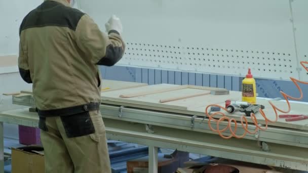 Ein männlicher Arbeiter klebt Holzrohlinge für eine Tür. Herstellung von Innentüren aus Holz — Stockvideo