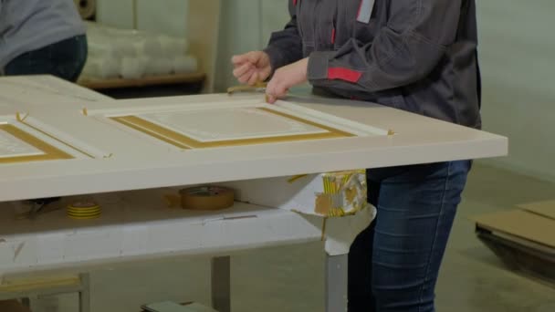 Eine Frau in einer Werkstatt klebt ein Schutzband an die Türe zur Herstellung von Innentüren aus Holz — Stockvideo