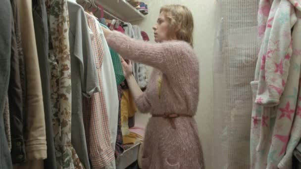 Vacker flicka leenden och går igenom galgar med kläder i sitt omklädningsrum — Stockvideo