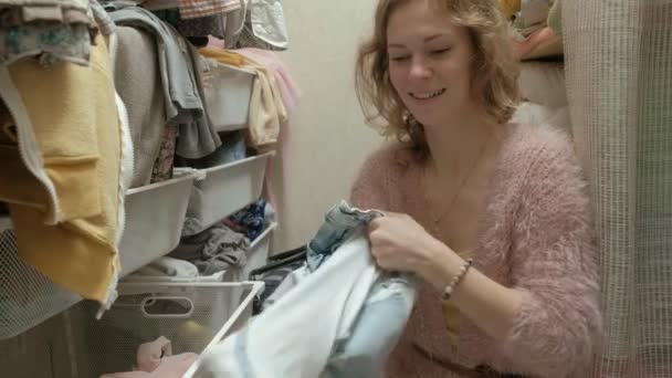 Lächelt ein schönes Mädchen, sortiert und faltet die Kleider in den Körben in ihrer Garderobe. bringt Ordnung in die Sache — Stockvideo