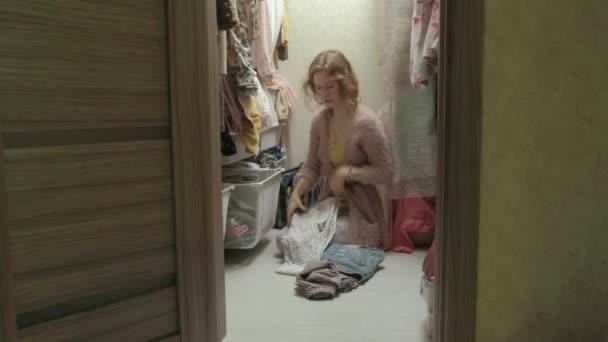 Una bella ragazza sorride, ordina e piega i vestiti nei cestini nel suo camerino. mette le cose in ordine — Video Stock