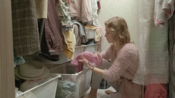 Een mooi meisje glimlacht, sorteert en plooien van de kleding in de manden in haar kleedkamer. Zet orde op zaken — Stockvideo