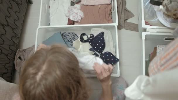 Uma linda garota sorri, sorri e dobra as roupas nos cestos em seu camarim. coloca as coisas em ordem — Vídeo de Stock