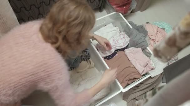 Een mooi meisje glimlacht, sorteert en plooien van de kleding in de manden in haar kleedkamer. Zet orde op zaken — Stockvideo