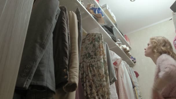Mooi meisje glimlacht en hangers met kleren doorloopt in haar kleedkamer. — Stockvideo