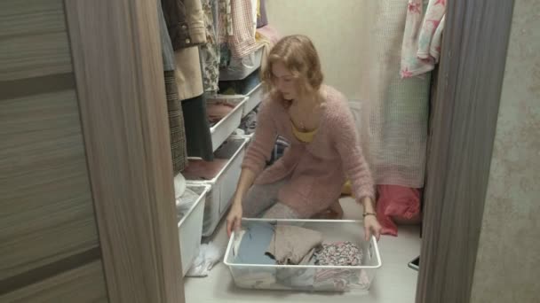 Красива дівчина посміхається, сортує і складає одяг у кошиках у своїй роздягальні. кладе речі в порядок — стокове відео