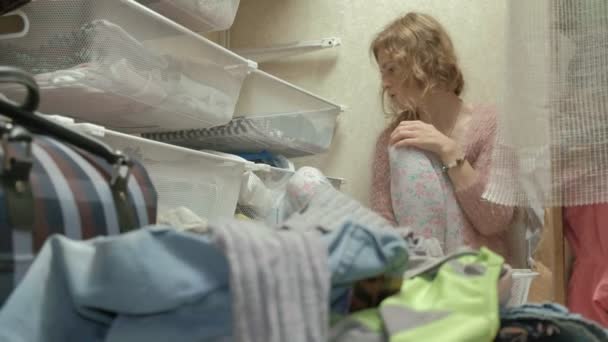 Kaunis tyttö on masentunut, väsynyt nuori äiti heittää vaatteita koreista pukuhuoneessaan. Järjestä asiat. — kuvapankkivideo