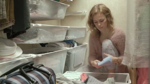 Uma menina bonita, uma jovem mãe pega e dobra roupas infantis em cestas em seu camarim. coloca as coisas em ordem — Vídeo de Stock