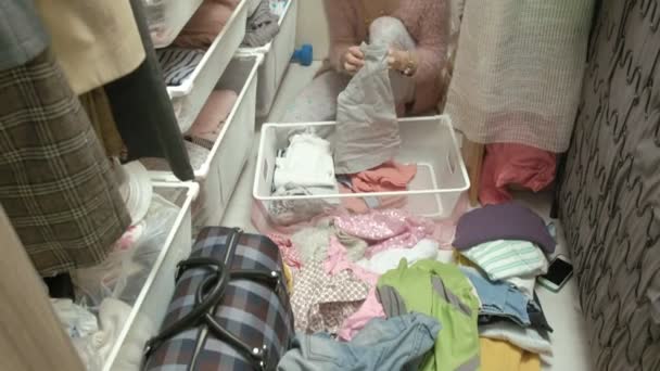 Piękna dziewczyna, młoda matka odbiera i fałdy Odzież dla dzieci w kosze w jej garderoba. stawia to w porządku — Wideo stockowe