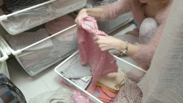 Una bella ragazza, una giovane madre raccoglie e piega i vestiti dei bambini in cestini nel suo camerino. mette le cose in ordine — Video Stock