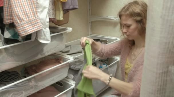 En vacker flicka leenden, sorterar och viker kläderna i korgarna i sitt omklädningsrum. sätter saker i ordning — Stockvideo