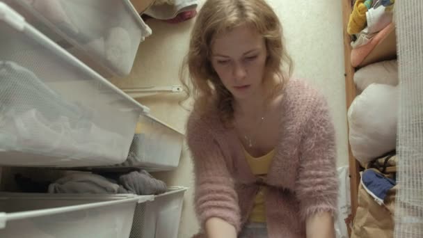 Ένα όμορφο κορίτσι, μια νεαρή μητέρα μαζεύει και διπλώνει παιδικά ρούχα σε καλάθια στο καμαρίνι της. βάζει τα πράγματα στη σειρά — Αρχείο Βίντεο
