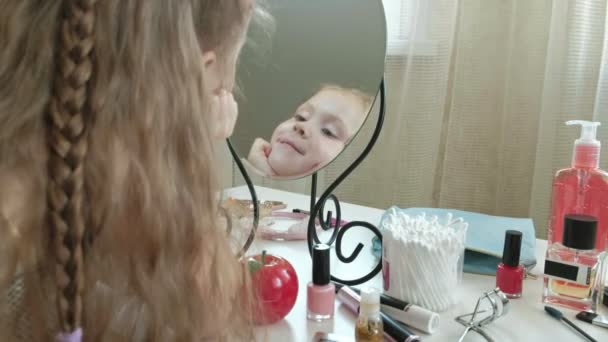 Μικρό κορίτσι με τα κόκκινα μαλλιά κοιτάζει στον καθρέφτη, χαμόγελα, μακιγιάζ, πρόσωπο, μόδα, στυλ, καλλυντικά — Αρχείο Βίντεο