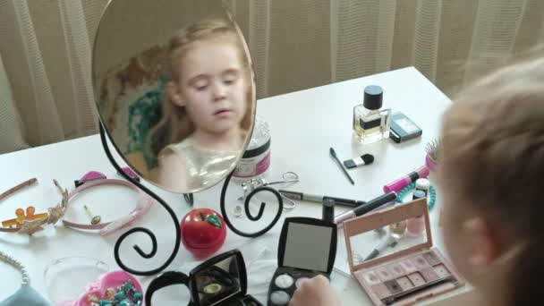 Маленькая девочка с рыжими волосами ставит тени на веки, смотрит в зеркало, макияж, лицо, мода, стиль, косметика — стоковое видео