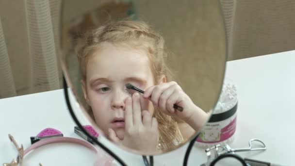 Маленькая девочка с рыжими волосами ставит тени на веки, смотрит в зеркало, макияж, лицо, мода, стиль, косметика — стоковое видео