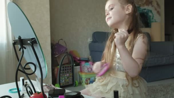 Μικρό κορίτσι με κόκκινα μαλλιά χτένες μαλλιών, κοιτάζει στον καθρέφτη, μακιγιάζ, πρόσωπο, μόδα, στυλ, καλλυντικά, περιποίηση των μαλλιών — Αρχείο Βίντεο