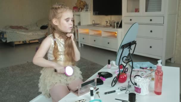Маленька дівчинка з рудим волоссям розчісує волосся, дивиться у дзеркало, макіяж, обличчя, мода, стиль, косметика, догляд за волоссям — стокове відео