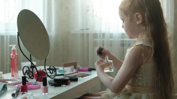 Ένα μικρό κορίτσι με τα κόκκινα μαλλιά ψεκάζει νερό άρωμα ή τουαλέτα, κοιτάζει στον καθρέφτη, μακιγιάζ, πρόσωπο, μόδα, στυλ, καλλυντικά — Αρχείο Βίντεο