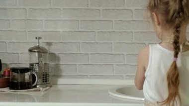 apronda güzel küçük kız bir sandalye üzerinde duruyor ve tablo mendil, çalışma yüzeyi parlak mutfakta anne yardımcı olur.