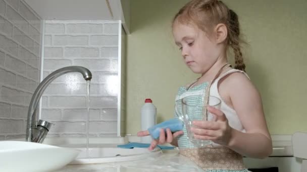 Belle petite fille dans un tablier est debout sur une chaise, dans la cuisine lumineuse, faire la vaisselle avec une éponge, aider les parents — Video