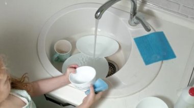apronda güzel küçük kız bir sünger ile veliler yardım bulaşıkları parlak mutfakta bir sandalye üzerinde duruyor