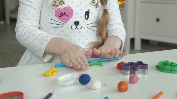 Uma menina brinca com plasticina, bolas de rolos, há figuras e lápis coloridos na área de trabalho, o desenvolvimento de habilidades motoras finas de mãos — Vídeo de Stock