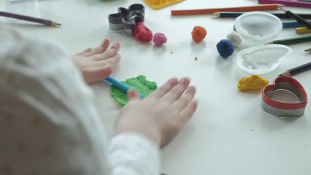 Ein kleines Mädchen spielt mit Knetmasse, rollt Kugeln, auf dem Schreibtisch liegen Figuren und Buntstifte, die Entwicklung der Feinmotorik der Hände — Stockvideo