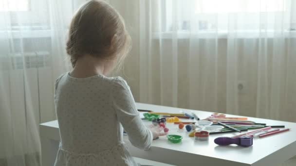 Uma menina brinca com plasticina, bolas de rolos, há figuras e lápis coloridos na área de trabalho, o desenvolvimento de habilidades motoras finas de mãos — Vídeo de Stock