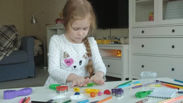Een beetje meisje speelt met plasticine, rolt ballen, er zijn cijfers en kleurpotloden op het bureaublad, de ontwikkeling van de fijne motoriek van handen — Stockvideo