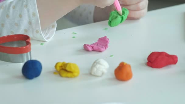 A little girl plays with plasticine, rolls balls, there are figures and colored pencils on the desktop, the development of fine motor skills of hands — Stock Video