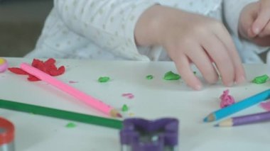 küçük bir kız oyun hamuru ile sculpts bir rakam, orada rakamlar ve renkli kalemler Masaüstü, ellerin iyi motor becerilerinin geliştirilmesi