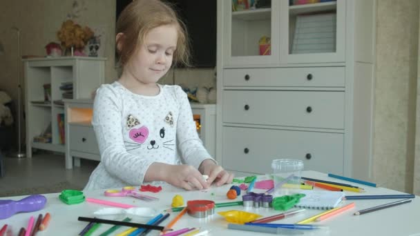 Felice bambina gioca con la plastilina, scolpisce una figura, sul desktop sono figure e matite colorate, lo sviluppo di abilità motorie fini delle mani — Video Stock